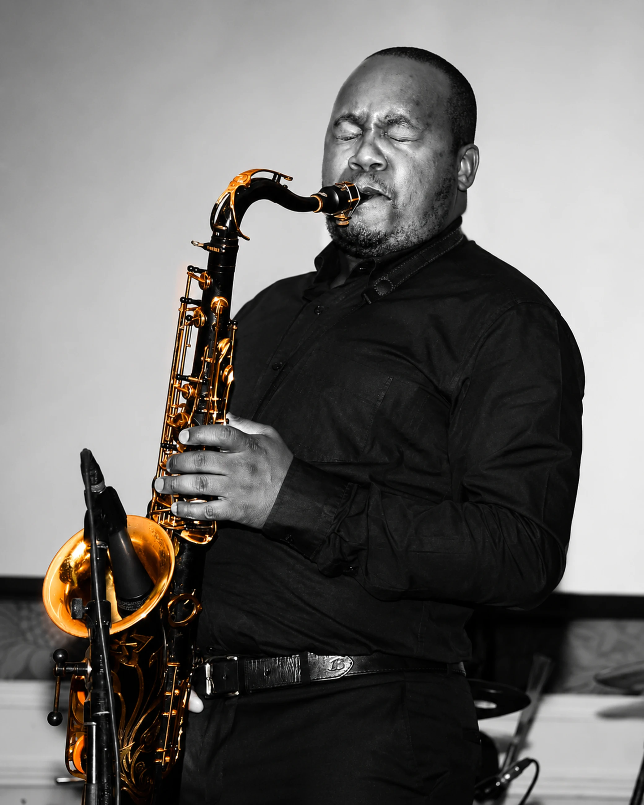 Edward Parseen in black against a pale backdrop, playing tenor saxophone