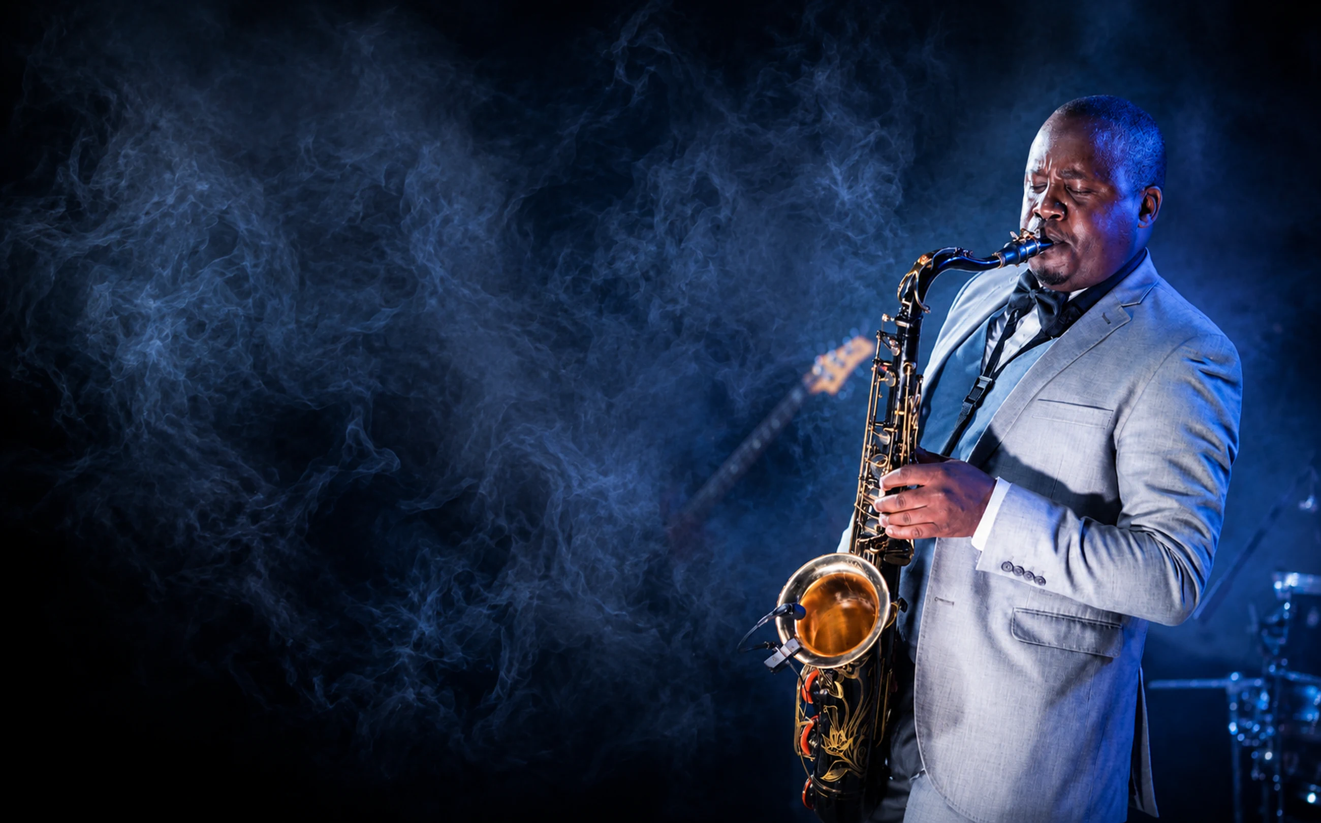 Edward Parseen in a grey suit and bow tie, playing under blue stage light