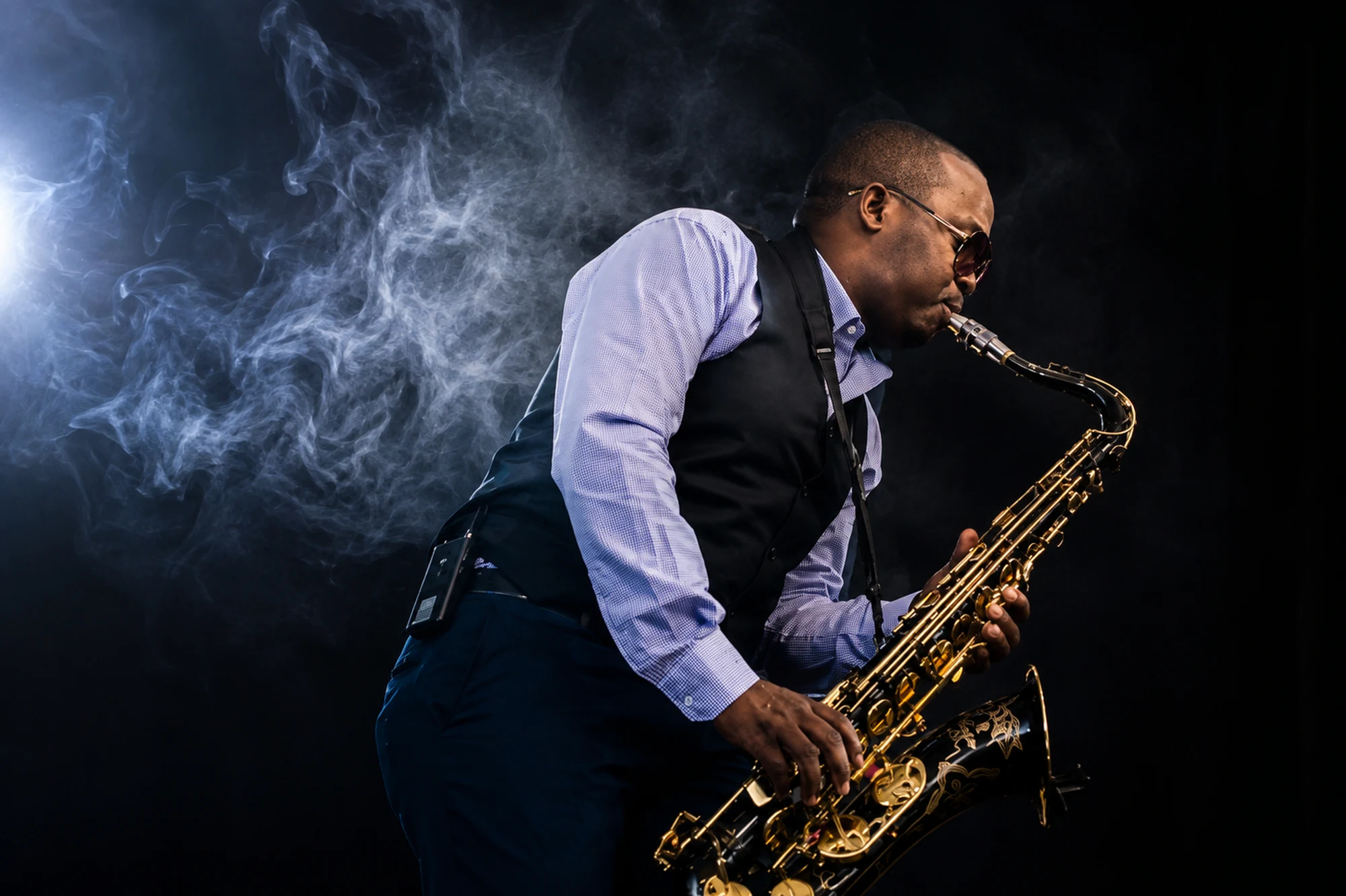 Edward Parseen playing tenor saxophone, lit from the side through smoke