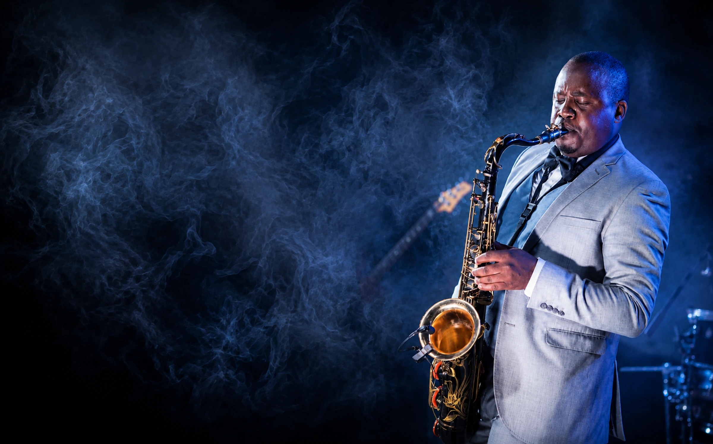 Edward Parseen playing saxophone in a grey suit under blue stage light